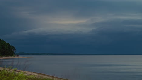 Storm-clouds-gather-over-beach-shoreline-by-forest-at-sunset-turning-to-blue-hour
