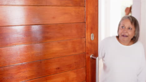 senior woman smiling and opening door, welcoming someone into her home