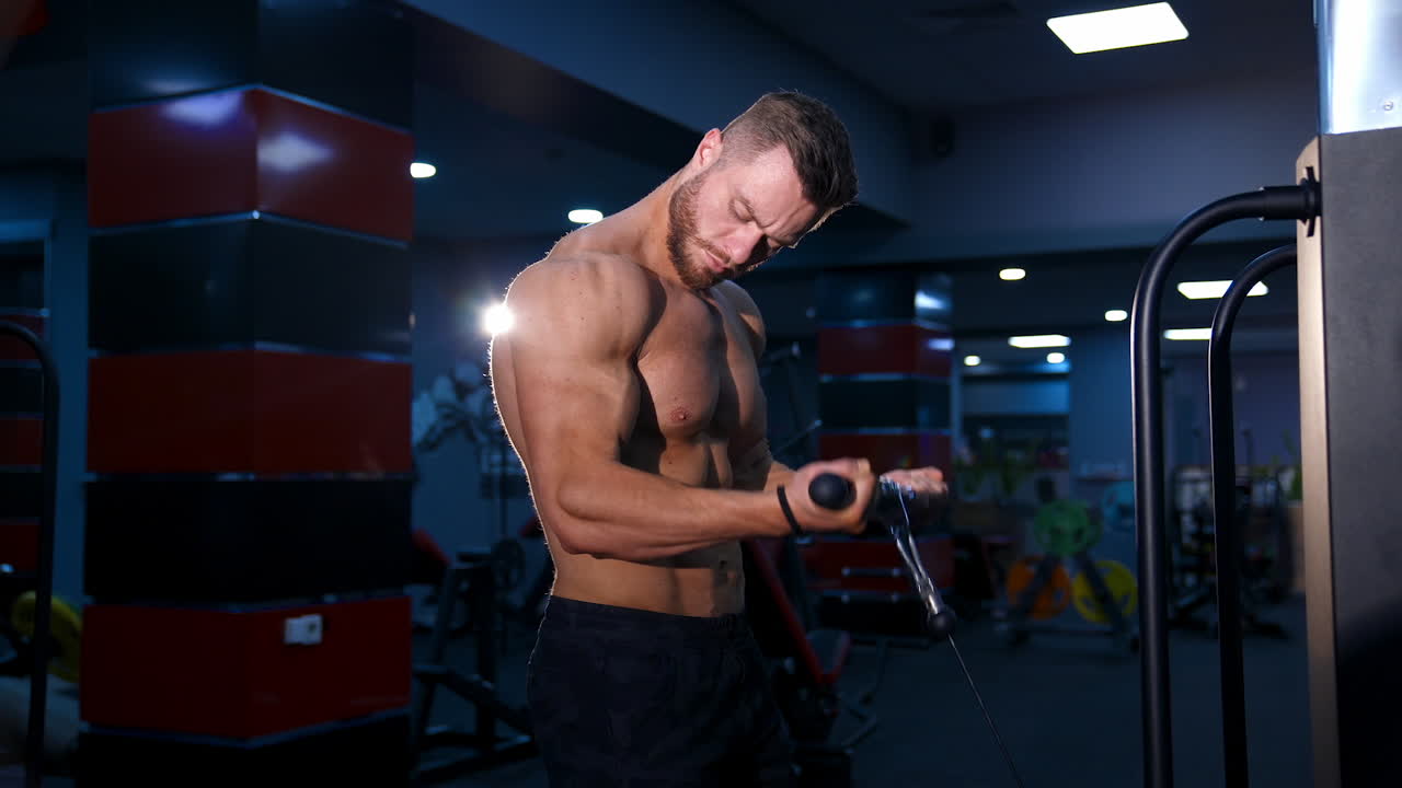Handsome fitness trainer doing workout for hands in gym. Modern equipment for sport. Slow motion.