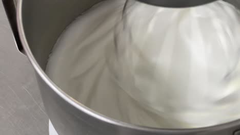 extreme close up to glossy, soft and fluffy meringue buttercream mixing in commercial grade electric mixer, baking preparation shot