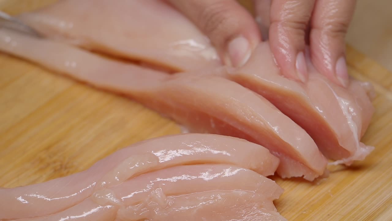 Mani che affettano pollo crudo su un tagliere di legno