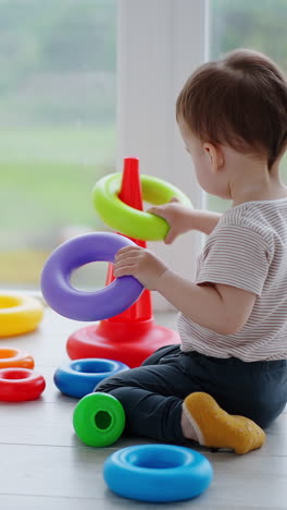 dark-haired toddler sitting on the floor busy with a toy. rear view of a child assembling the pyramid.. vertical video