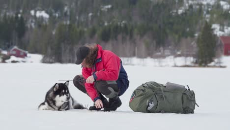 perro acostado al lado de un tipo atrapando pesca a través de un agujero de hielo en un lago congelado
