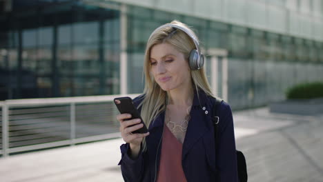 portrait of young lively blonde business woman intern happy listening to music wearing headphones texting browsing social media using smartphone