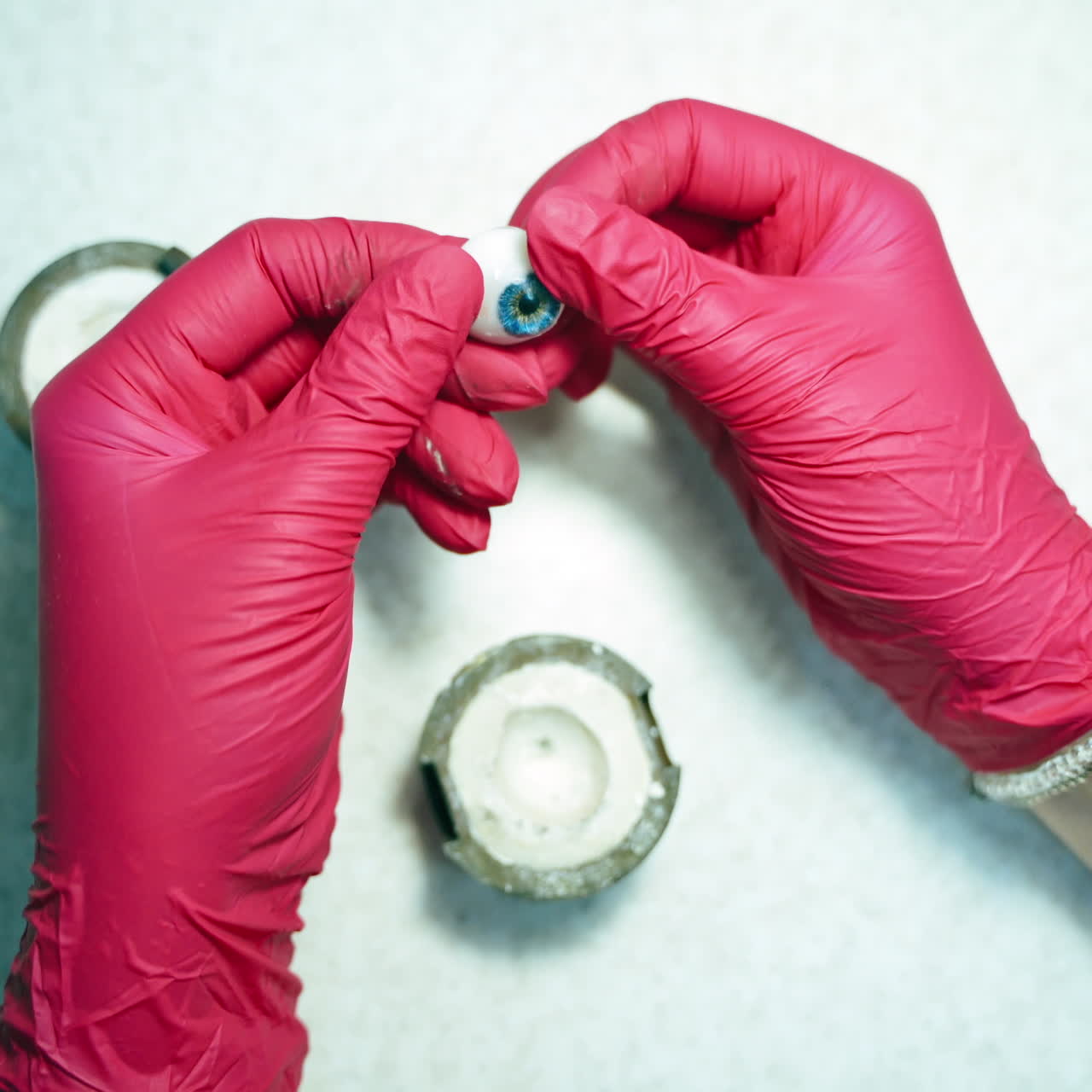 Technician opens the box and looks at artificial eye. Hands in red gloves taking out ready eye prosthesis.