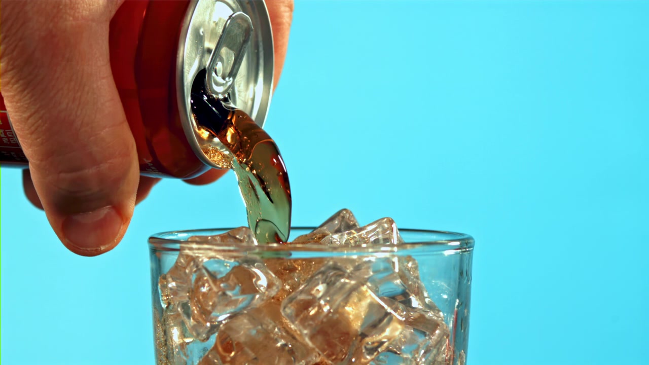Versamento al rallentatore di Coca-Cola da lattina rossa in un bicchiere con ghiaccio
