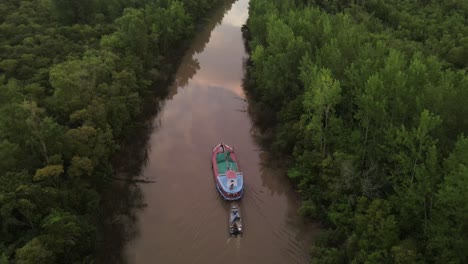 toma cinematográfica de drones de un barco que transportaba un bote pequeño en el río amazonas rodeado de árboles verdes de la selva tropical durante el amanecer