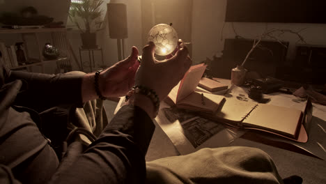 man holding illuminated crystal ball in a cozy study