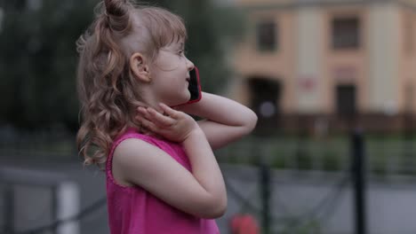 niña hablando por teléfono inteligente al aire libre. niño con vestido rosa hablando por teléfono móvil en la calle de la ciudad