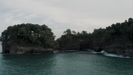 Impresionantes-Paisajes-De-Olas-Rompiendo-En-Una-Isla-Rocosa-Con-Una-Densa-Vegetación