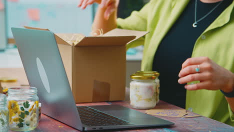 Mujer-Con-Computadora-Portátil-Ejecutando-Negocios-En-Línea-Desde-Casa-Empacando-Velas-Boutique-Para-Su-Envío