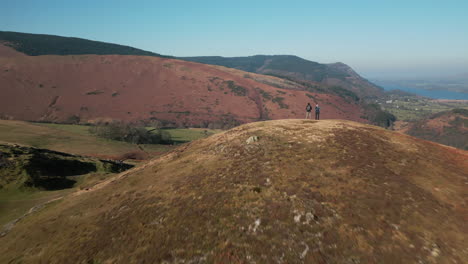 Flying-past-hikers-on-hilltop-revealing-valley-beyond-in-winter-in-English-Lake-District-UK