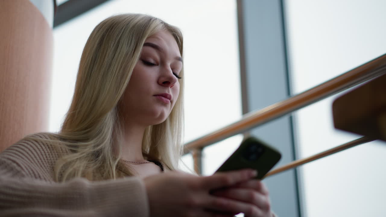 Close-up of woman seated operating her phone, looking left and right, possibly checking messages or notifications, with soft focus on phone and hands