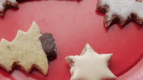 a leftward pan over christmas-themed german butterplätzchen on a red plate, featuring cookies shaped as a shooting star, star, and tree, capturing festive charm and crumbly texture