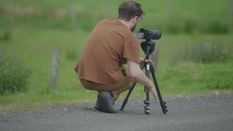 jonge mannelijke squatting down bereidt zijn camera en statief apparatuur om te schieten