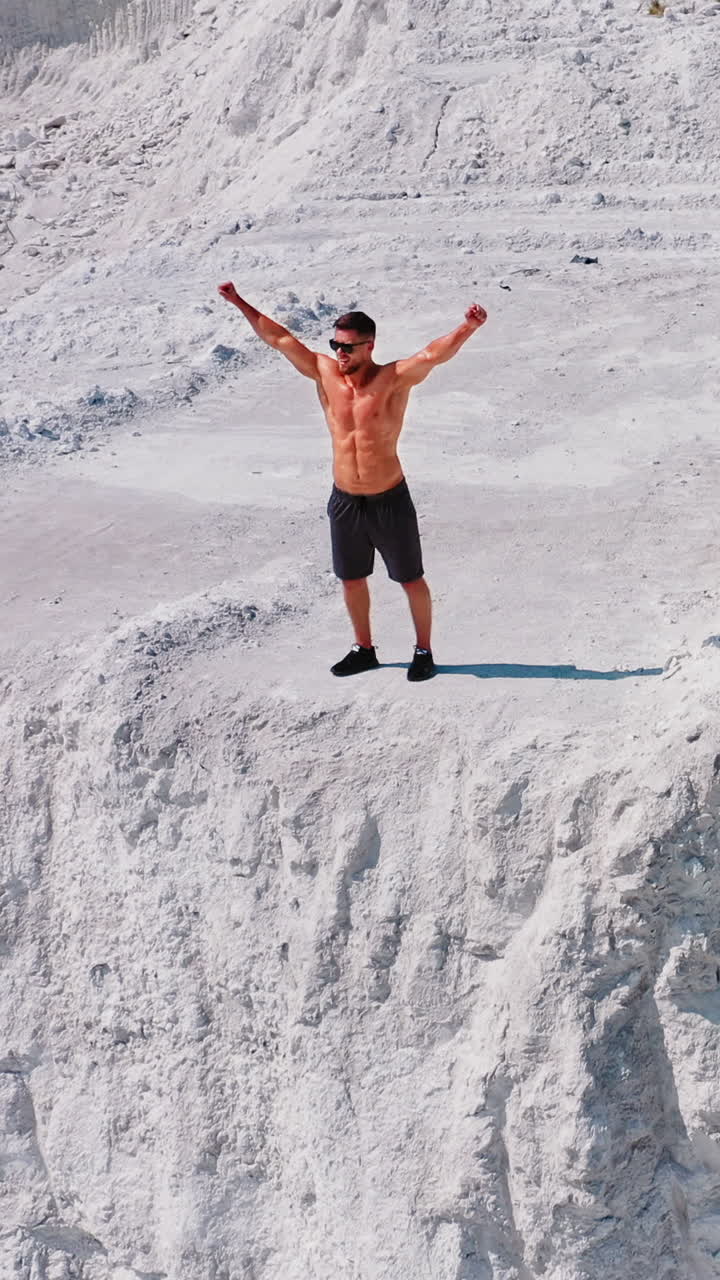 Healthy man running on white canyon. Shirtless athlete training happily on beautiful natural background in summertime. Aerial view. Vertical video