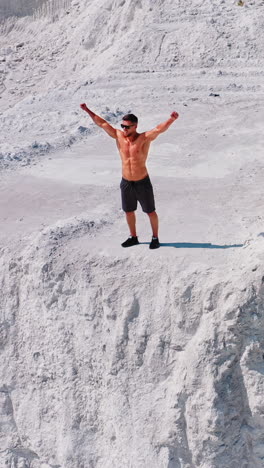 healthy man running on white canyon. shirtless athlete training happily on beautiful natural background in summertime. aerial view. vertical video