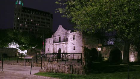 The-Alamo-at-night-in-San-Antonio,-Texas-with-gimbal-video-walking-sideways-by-trees