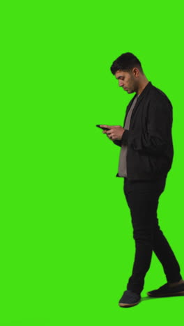 video vertical de larga duración de un joven caminando en el marco de mensajes de texto en el teléfono móvil de pie contra la pantalla verde