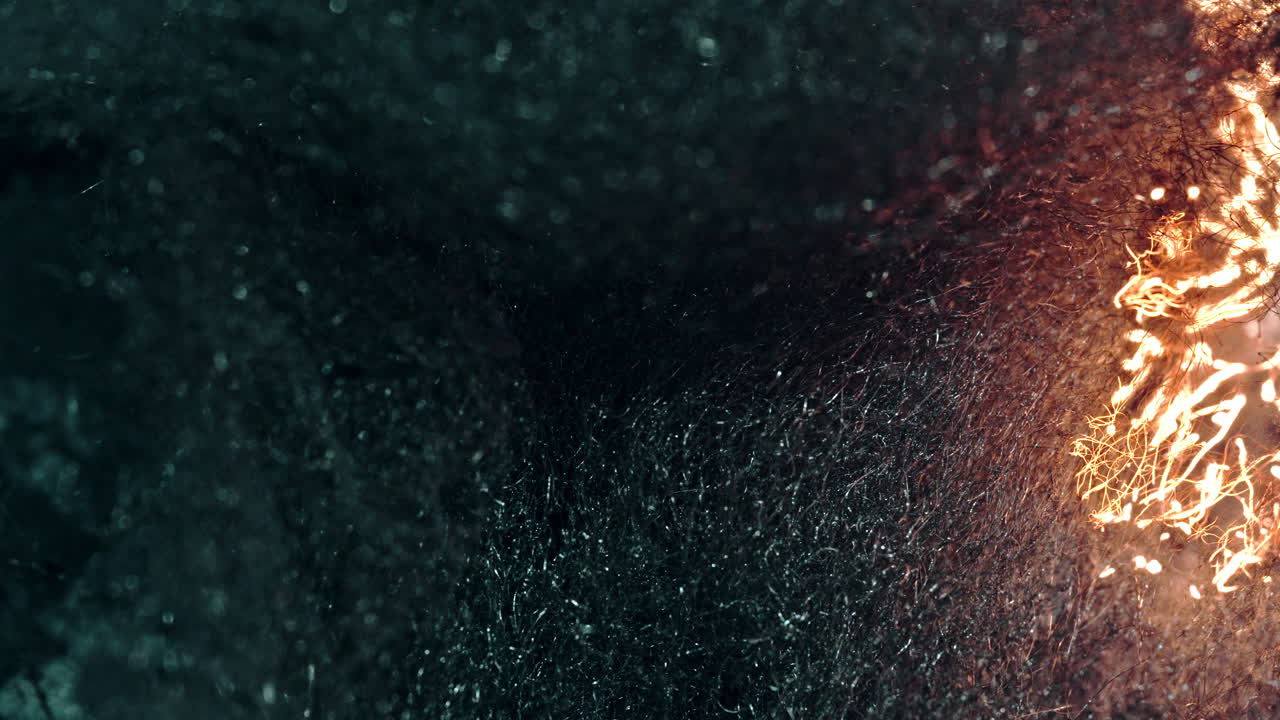 A close-up of a dark, textured surface, as fire burns through it, creating sparks
