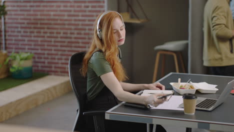 young caucasian business woman writing notes using smartphone checking messages enjoying study listening to music wearing headphones female student in diverse office workplace