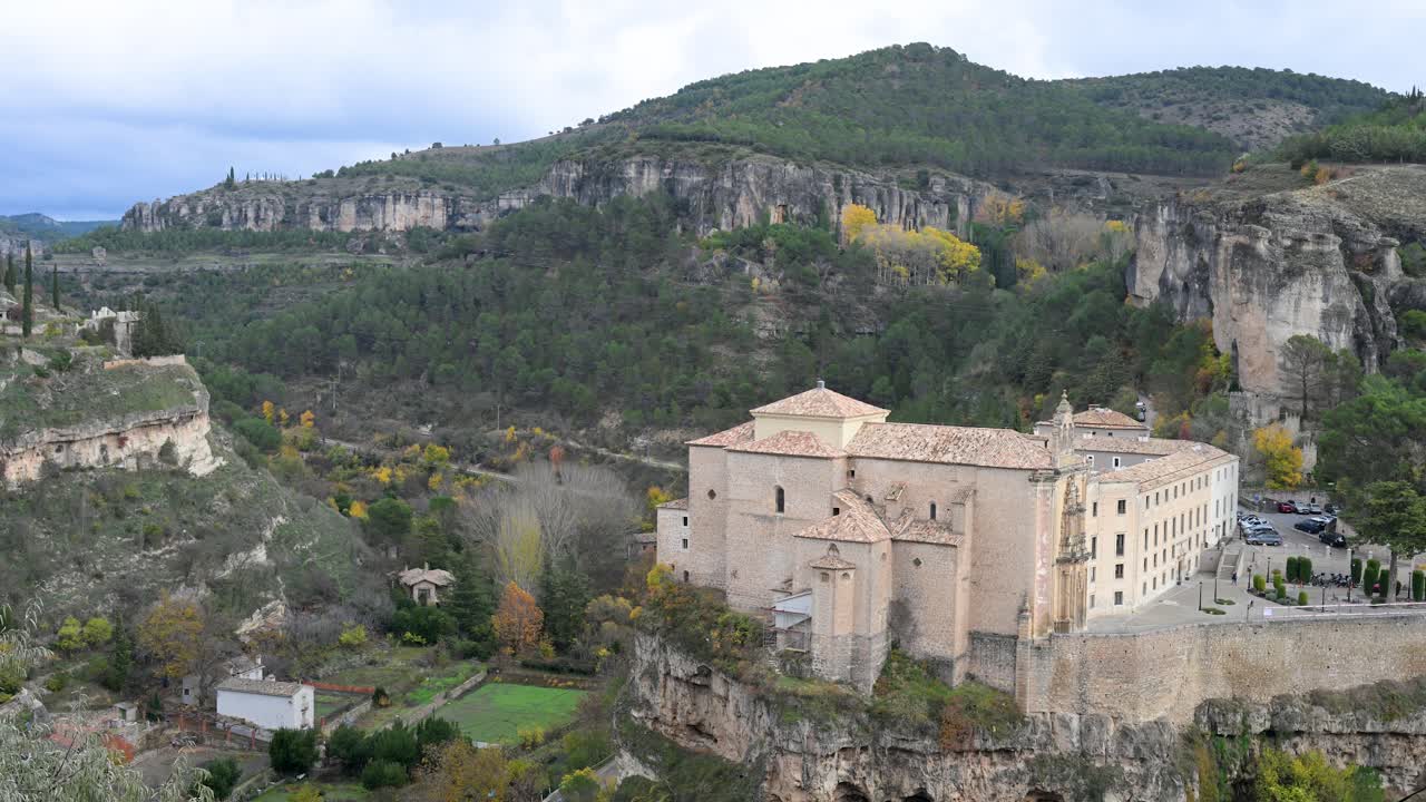 CUENCA, SPAIN - The historic Parador de Cuenca, a former convent, stands majestically on a cliff, offering views of the gorge and hills in vibrant autumn color.