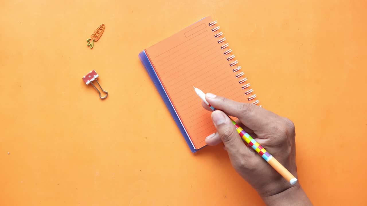 escritura a mano en un cuaderno de notas en espiral naranja en una superficie naranja