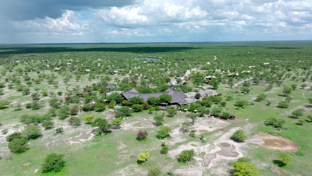 Vista aérea de exuberantes llanuras de sabana verde cerca de Etosha, en el norte de Namibia, con arbustos dispersos y claros que se extienden bajo un cielo brillante lleno de nubes.