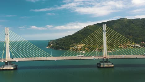 drone aerial side panning view of concrete cable-stayed bridge traffic above turquoise color ocean