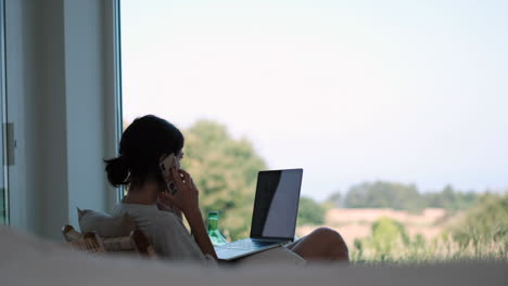 freelancer lifestyle: young woman balancing work and relaxation on phone with laptop in sunlit room