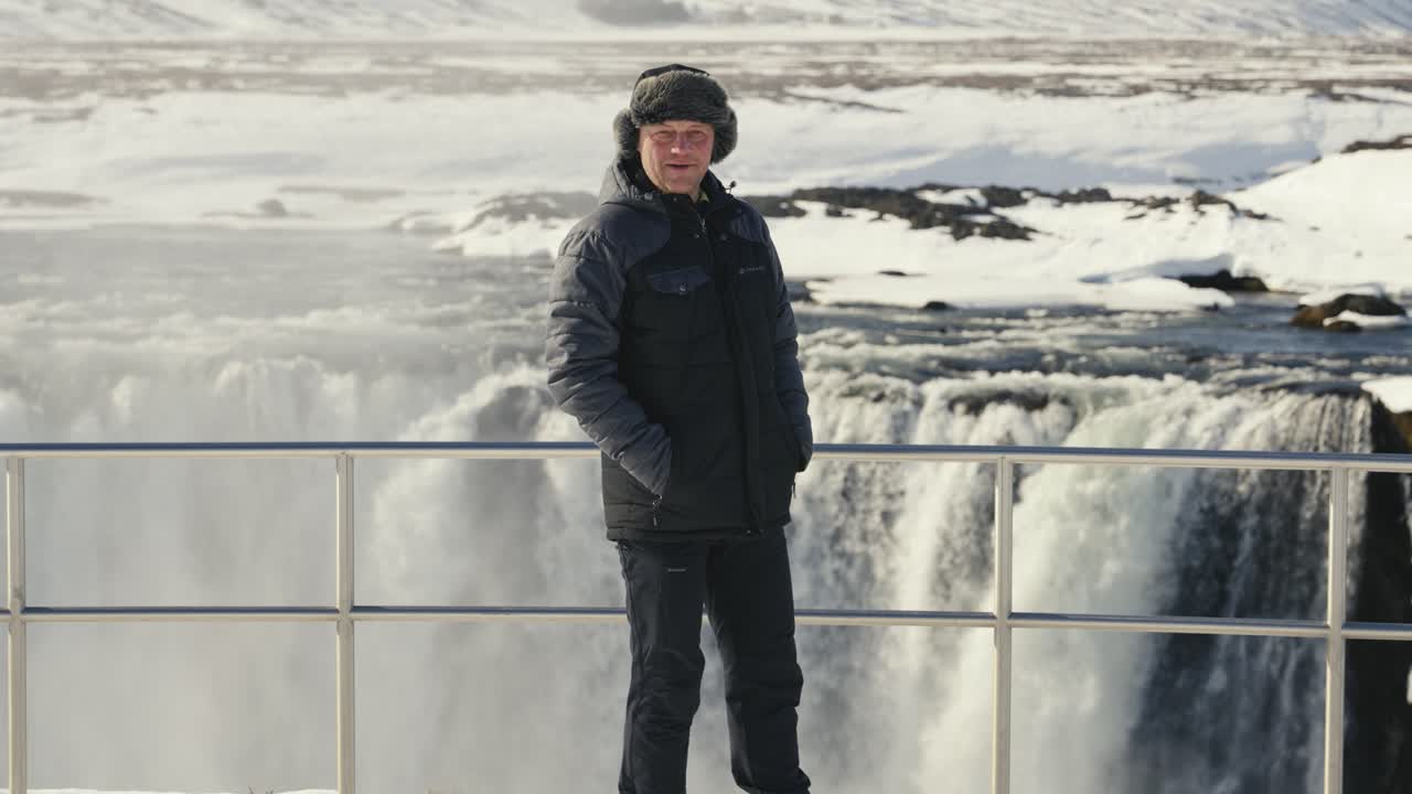 Adult male stand near Godafoss waterfall metal safety barrier sightseeing area