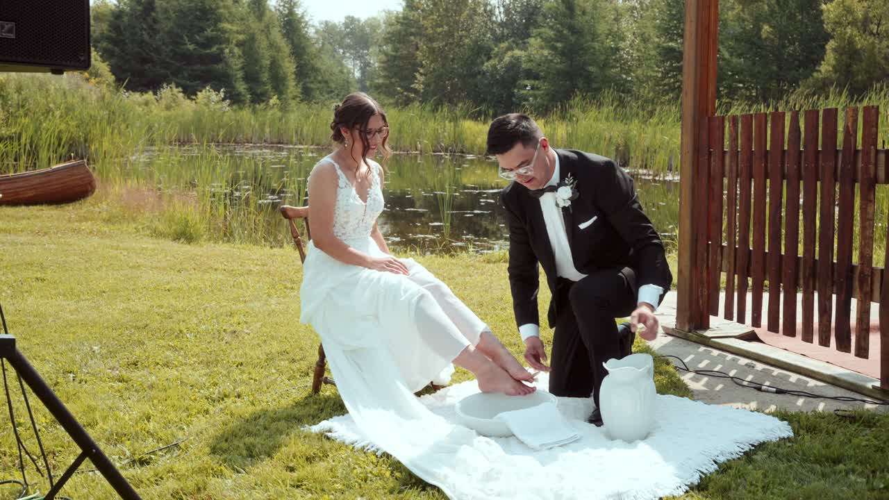 Groom kneels to remove bride’s shoes and bathe her feet during outdoor vows