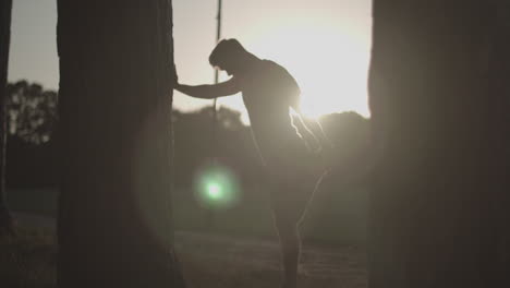 man in park stretches out legs before going for a run whilst being silhouetted by the sun