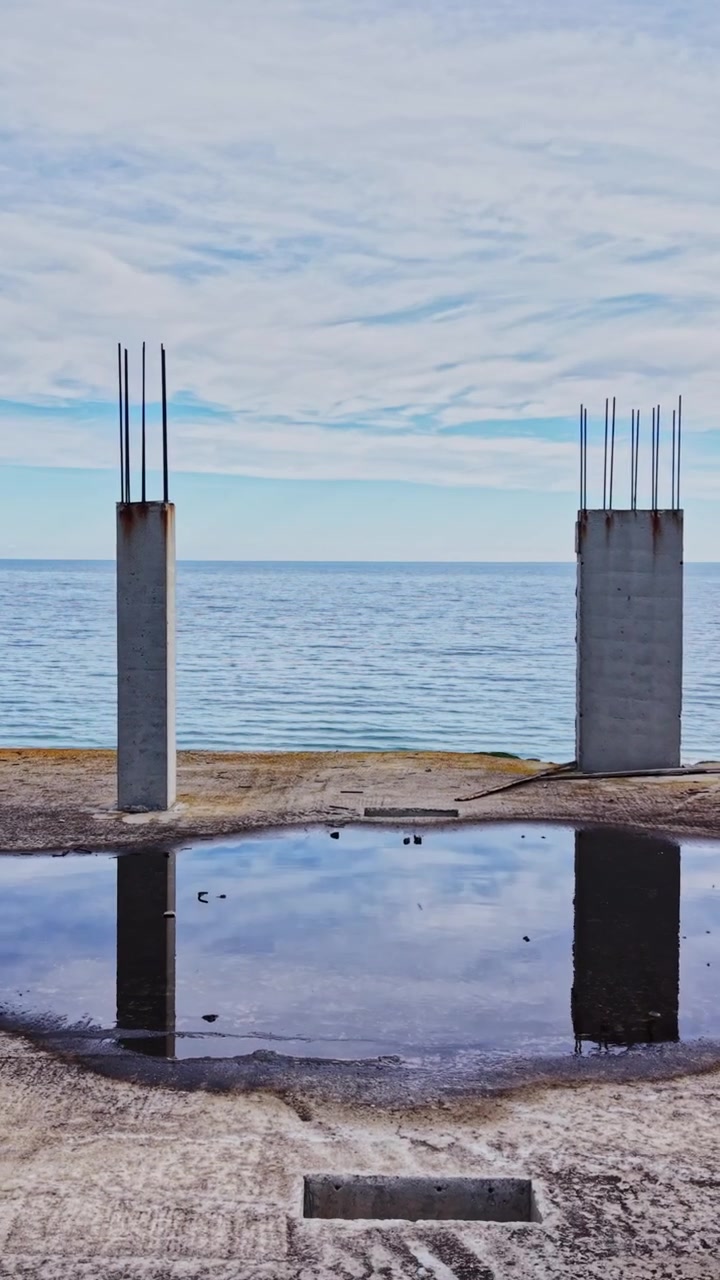 Construction site overlooking the ocean with concrete pillars and farmland