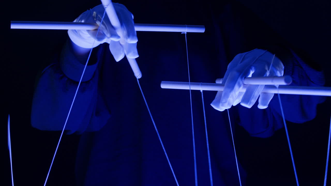 Hands in White Gloves Manipulating Puppet Strings Under Blue Light