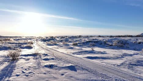 Sol-Brillando-Sobre-Una-Remota-Carretera-Cubierta-De-Nieve,-Aproximación-Aérea-Hacia-Adelante