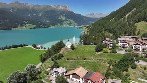 vista aérea de uma paisagem cênica com uma área residencial e um lago sereno em campanile di curon venosta vecchia, no tirol do sul, itália