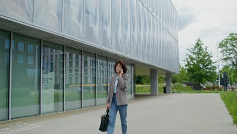 mujer de negocios caminando y hablando por teléfono cerca de un edificio moderno