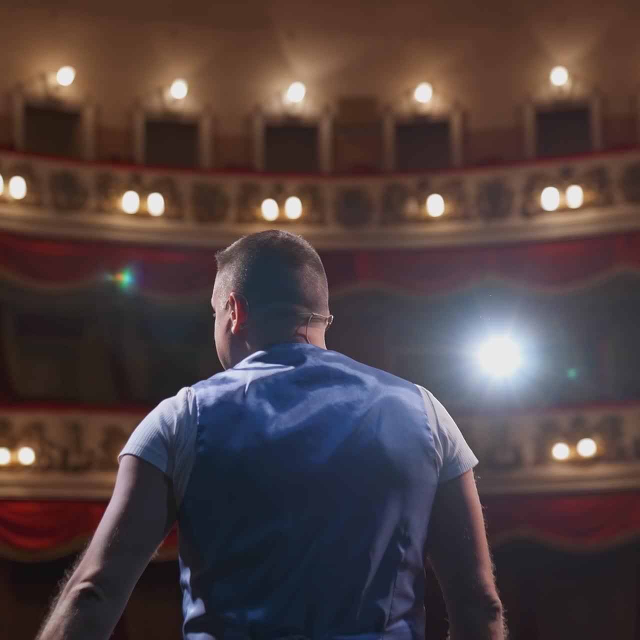 Male actor on classic theatre stage. Actor is speaking and turning around in spotlights during the performance. Cinematic back view shot.