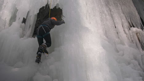 Vista-De-ángulo-Bajo-De-Un-Escalador-De-Hielo-Que-Aborda-Una-Enorme-Pared-De-Hielo