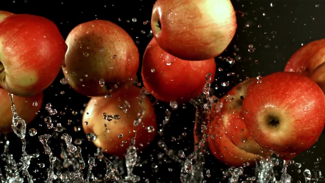 Mele rosse fresche che schizzano nell'acqua su uno sfondo nero al rallentatore