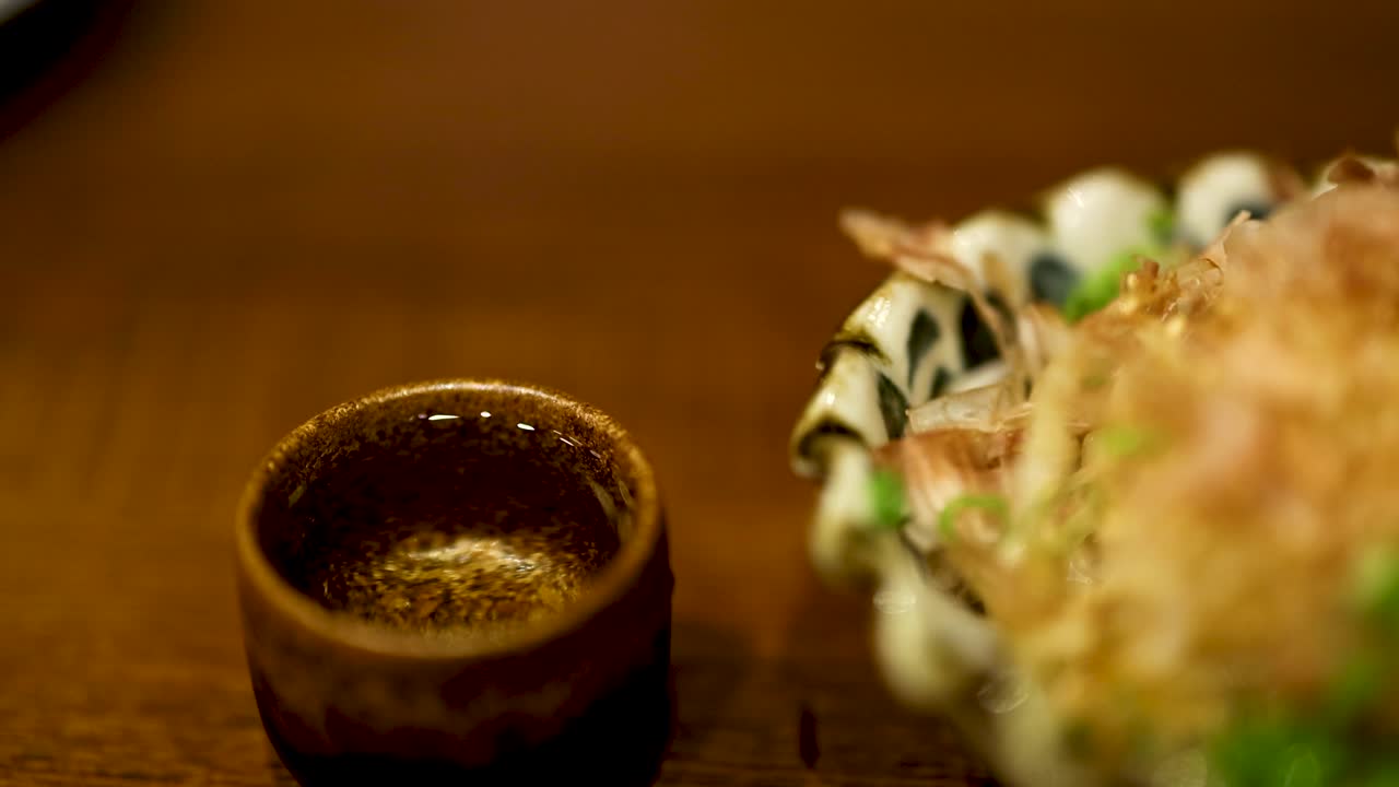Hand reaching for sake cup beside food
