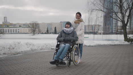 happy muslim woman taking her disabled friend in wheelchair on a walk around the city in winter