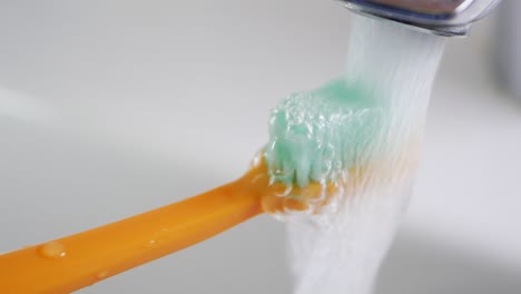 close-up of a toothbrush being rinsed under running water in a sink