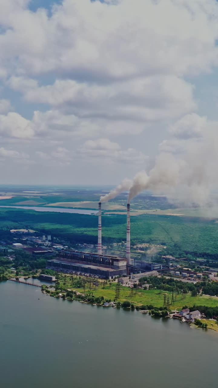 Natural environment of fields, forests, a wide river and factory polluting the air. Pipes with smoke from the big plant near the river. Ecological problem. Vertical video
