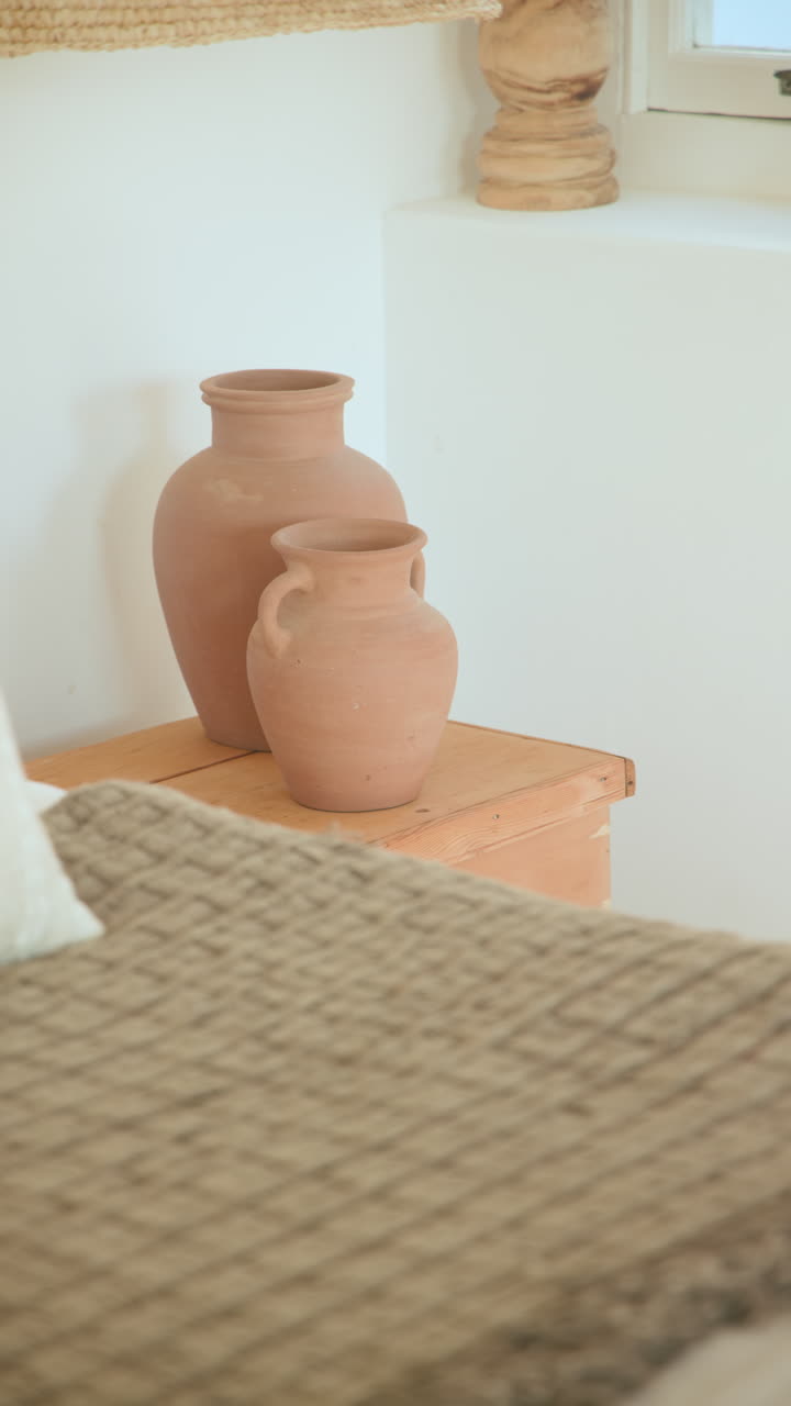 Vertical video: Cozy bedroom with textured blanket and decorative clay vases on wooden table