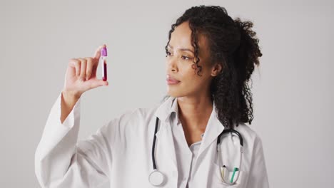 Video-of-biracial-female-doctor-holding-test-tube-on-white-background