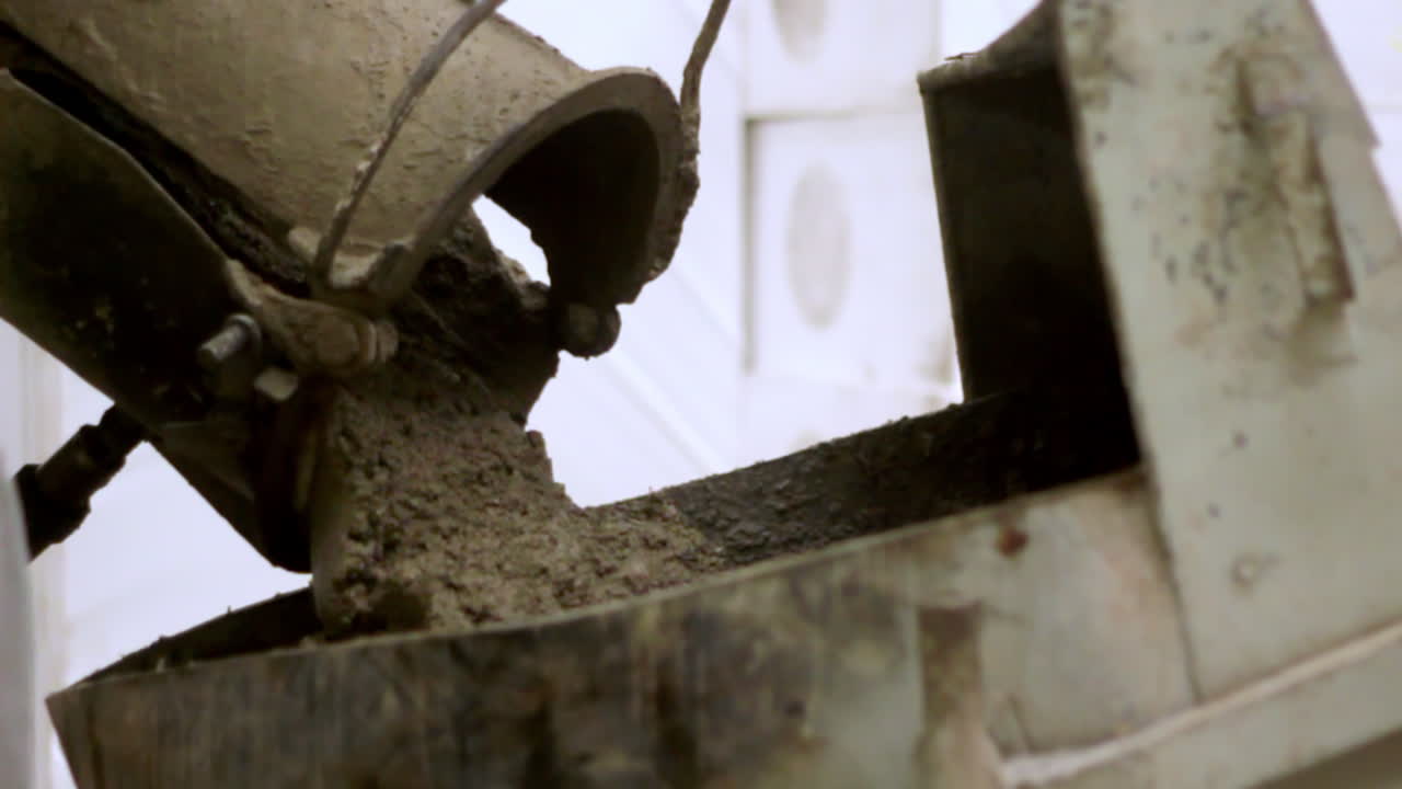 Close-up of wet concrete being poured from a cement mixer chute into a metal container at an industrial construction site, showing texture and motion in the pouring process.