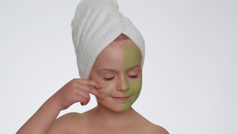 Beautiful-smiling-child-girl-kid-in-towel-on-head-applying-cleansing-moisturizing-green-mask-on-face