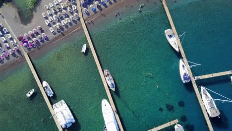drone flying over small harbour with boats, beach and swimming people